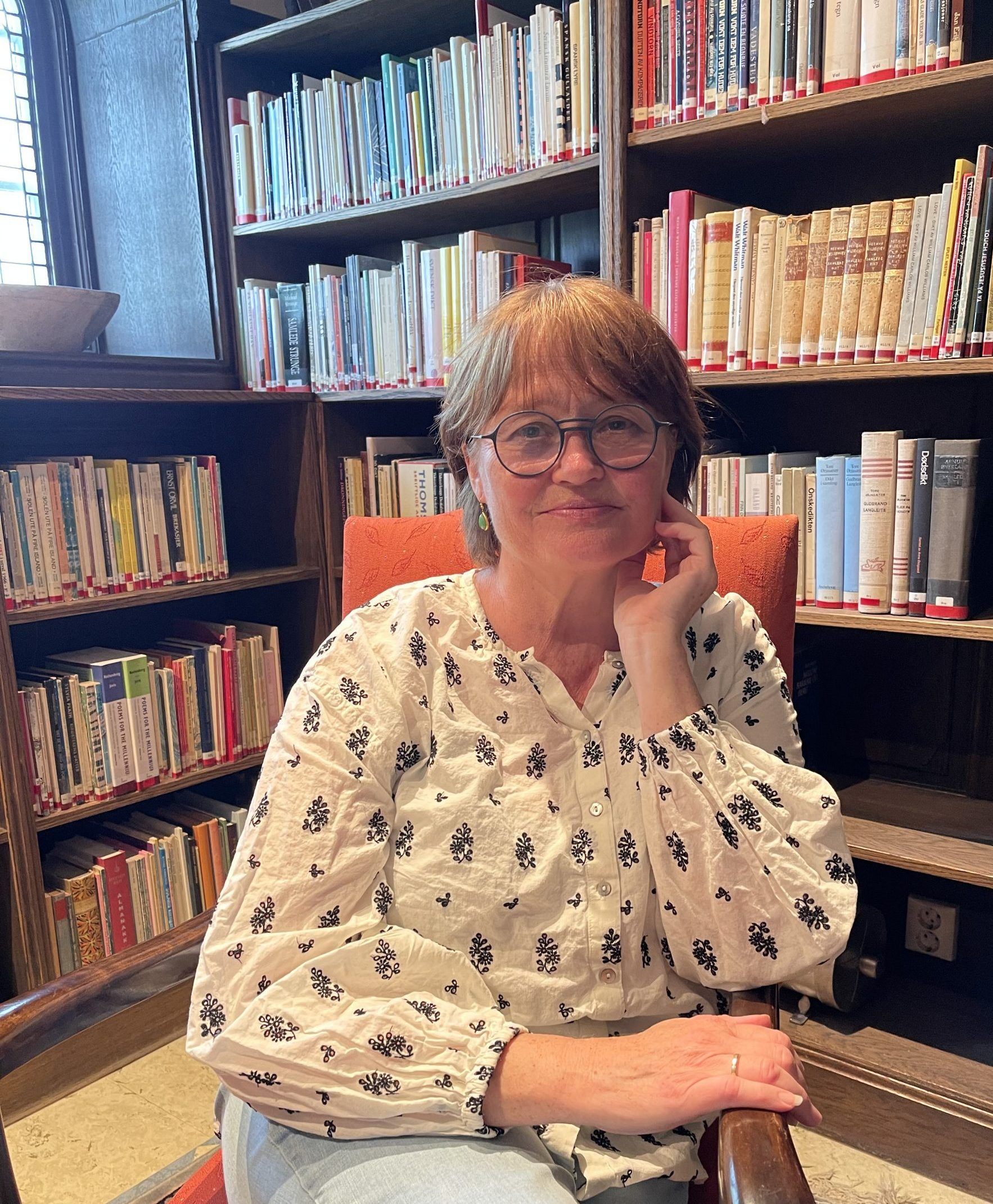 Unn Irene Aasdalen i rød stol med bokhyller bak
