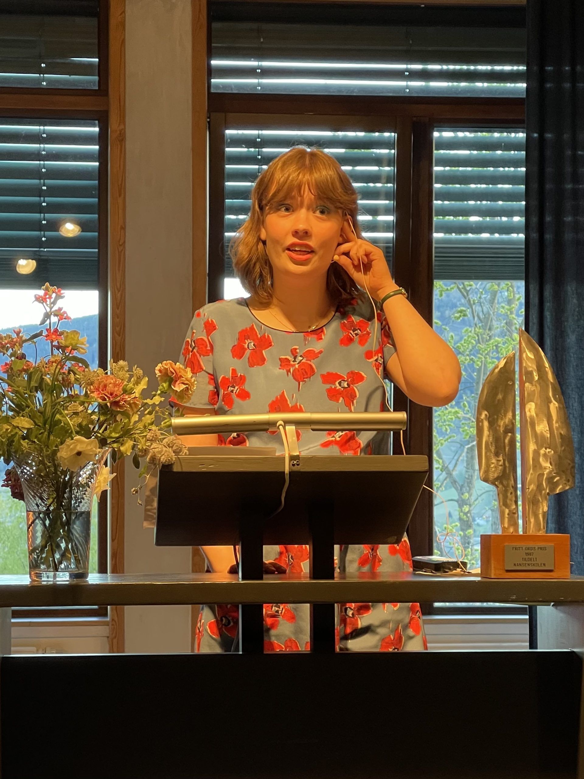 Ung kvinne med blomstrete kjole holder tale ved nansenskolens talerstol