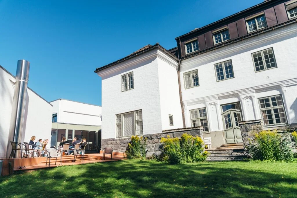 Liten gruppe sitter utenfor Nansenskolen i solskinnet