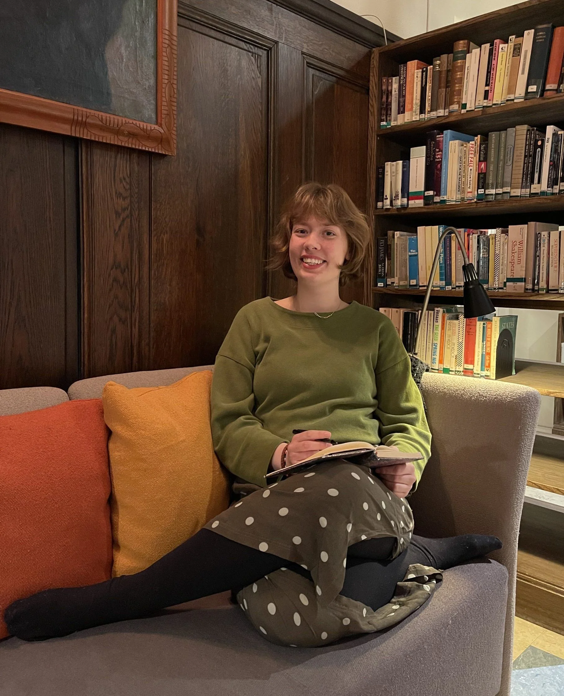 Student sitter og skriver i bok i sofa foran bokhylle
