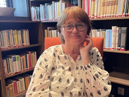 Unn Irene Aasdalen i rød stol med bokhyller bak